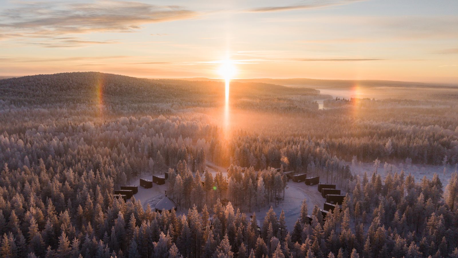 Luchtfoto van glazen iglo’s in Lapland bij Halo Igloos, met de winterzon boven het sneeuwbos