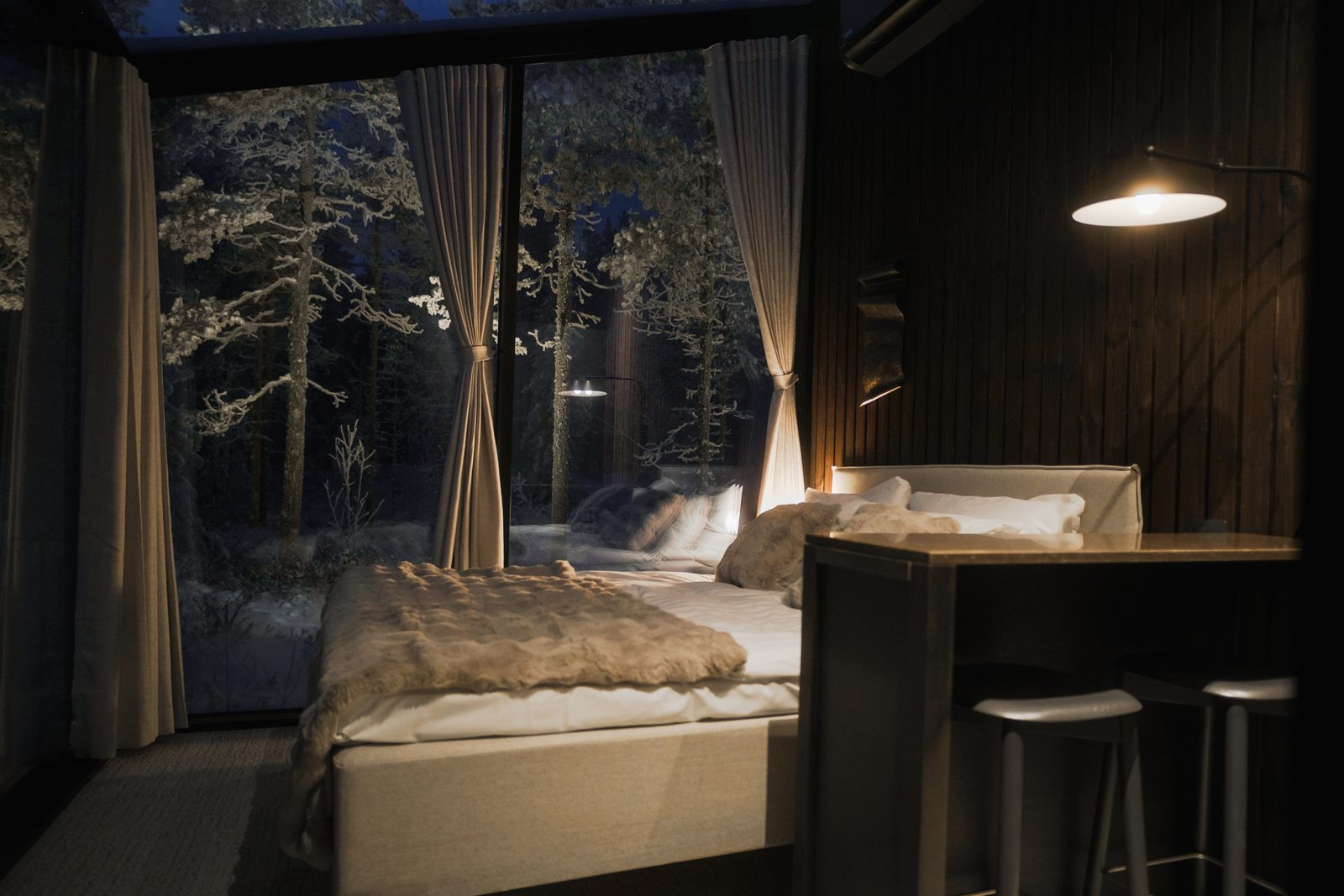 Interieur van een glazen iglo in Lapland met tweepersoonsbed en uitzicht op het besneeuwde bos